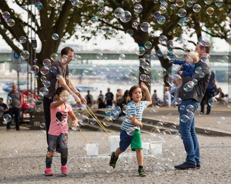 Children chase bubbles below in a riverside park in Cologne.