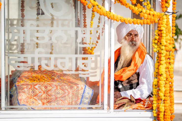 Old man with beard and turban in a glass box covered with marigold garlands