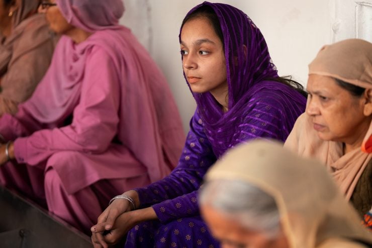 Women sit around a wash bin wearing bright colors